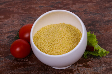 Raw couscous in the bowl served salad leaves, tomato and pepper