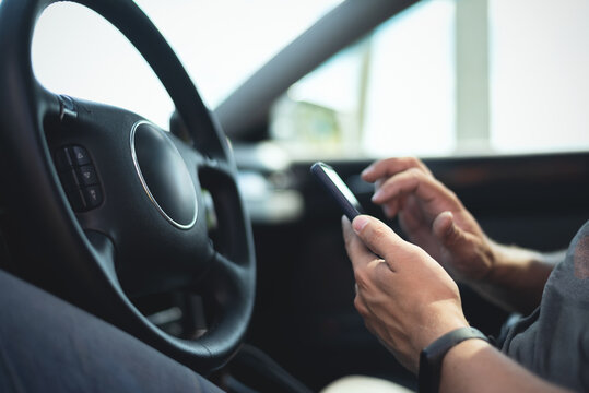 Driver with mobile phone is sitting by a steering wheel of car.