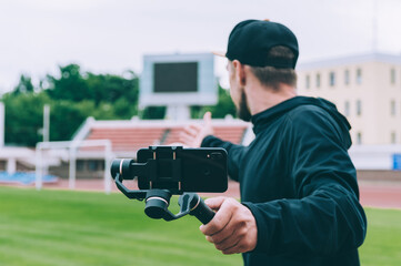 Blogger in the stadium shoots video on a smartphone with a manual camera stabilizer.