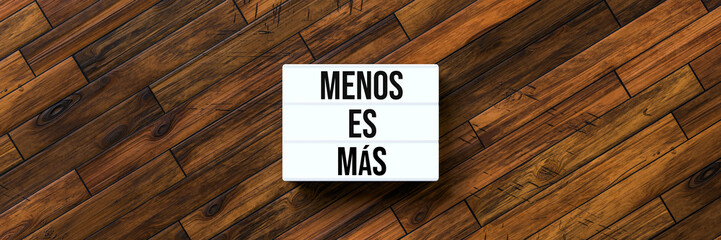 lightbox with Spanish message for LESS IS MORE on wooden background