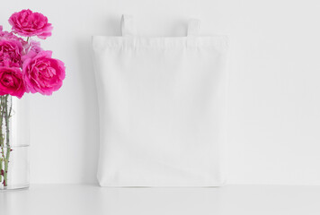 White tote bag mockup with a bouquet of a roses on a white table.