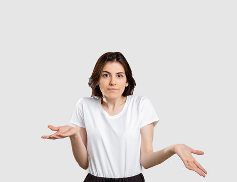 Shrug gesture. No idea. Confused woman raising shoulders isolated on neutral background.