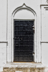 Black, metal-bound door of white-stone residential chambers of the XV century