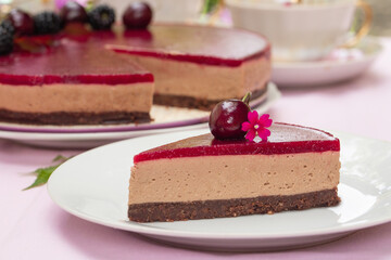 A piece of No-bake chocolate mousse cake with sweet cherry  jelly, decorated with sweet cherries and flowers on pink table cloth. Teatime in the garden.