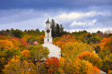 White country church and American flag surrounded by autumn colors in New England