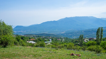 Beautiful view to green valley village and summer rocks mountains against blue sky. Concept of hiking and traveling. Solo outdoor activities. Copy space, natural background