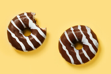 Two chocolate donuts on a yellow background.
