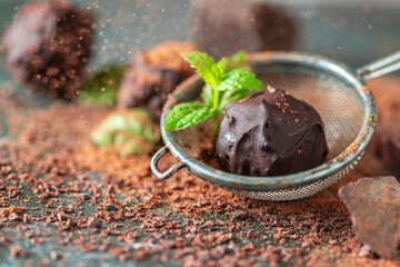 Delicious chocolate truffles with mint, cocoa powder and dark chocolate on a dark wooden background.