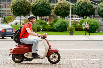Side view on a man is riding on a scooter in the city - obrazy, fototapety, plakaty