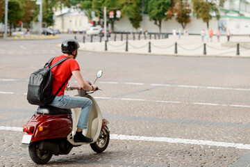 Fototapeta na wymiar Man, with a backpack and helmet, is driving a scooter