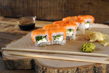 Philadelphia roll sushi with salmon, prawn, avocado, cream cheese. Wasabi and chopsticks on a wooden board. Japanese food.