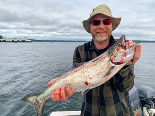 Smiling man holds bloody Chinook salmon fish on a Puget Sound, Washington fishing trip