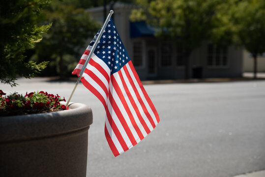 A Small American Flag placed on the side of the street in a small town.
