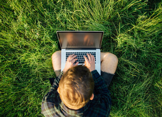 Overhead view of hipster student using empty screen laptop on grass in park at sunset