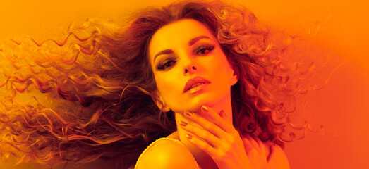 High Fashion. Woman in colorful neon gold light, make-up. Sexy blond girl, stylish curly hair, trendy makeup. Golden neon portrait. Creative beauty, fashionable model face, voluminous hairstyle