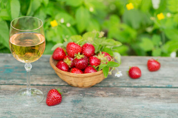 Glass of rose wine served with fresh strawberries on wooden background. Picnic outdoor with pink wine and berries.