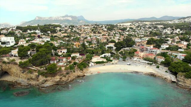 Distant aerial view rocky coves, sandy beach, tiny bay of Benissa. Turquoise bright blue Sea waters hillside townscape at sunny day. Drone point of view. Costa Blanca. Spain..