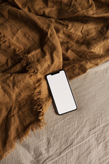 Blank screen mobile phone on brown, beige blanket. Flat lay, top view. Copy space mockup template.
