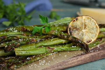 Oven baked asparagus served with lemon and parsley on blue wooden board, closeup