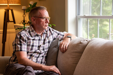 Mature man looking out living room window on a rainy day.