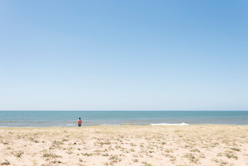 Obraz premium Uruguay beach in summer, young man seen from behind looking at the sea.