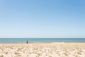 Uruguay beach in summer, young man seen from behind looking at the sea.