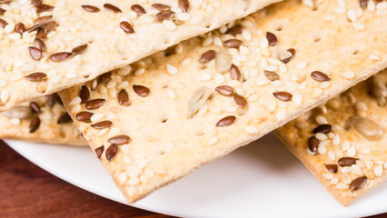 crispy wheat cakes with sesame seeds, flax and sunflower on plate on red wooden background. vegetarian food, eco food concepts