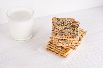 Stack of crispy wheat cakes with sesame, flax and sunflower seeds on on a napkin on white wooden background   with glass of milk. vegetarian food, eco food concepts