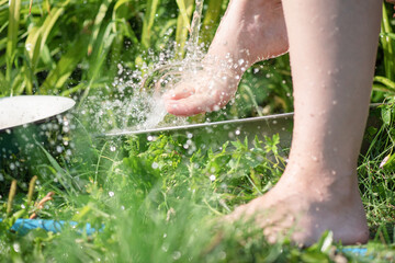 Woman is washing her legs under a water from water hose in a garden.
