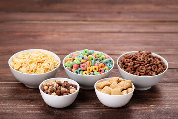 Various corn flakes in bowls on brown wooden table