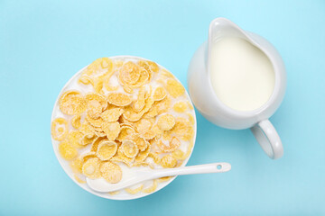 Corn flakes in bowl with milk and spoon on blue background