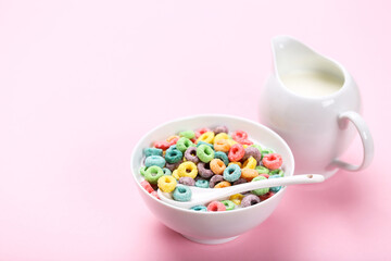 Colorful corn rings in bowl with milk and spoon on pink background