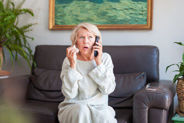 An elegant woman looks in surprise at the phone while sitting on a sofa in her house.