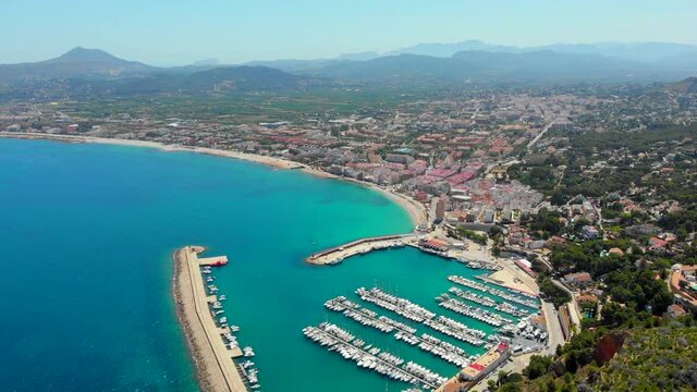 Aerial drone point of view coastal town of Javea with green mountains, turquoise bay Mediterranean Sea moored vessels in harbour, comarca of Marina Alta in province of Alicante, Valencia, Spain