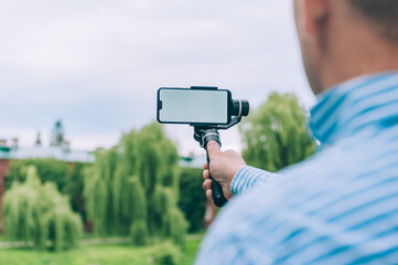Blogger in nature shoots video on a smartphone with a manual camera stabilizer.