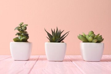 Artificial plants in white flower pots on pink wooden table