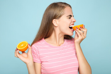 Young girl eating fresh orange fruit on blue background