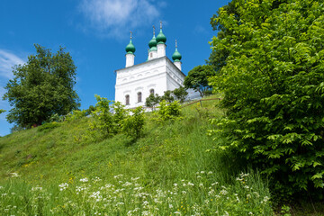 A snow-white church with green domes on the edge of a high cliff.