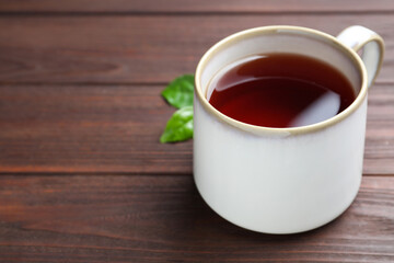 Cup of aromatic black tea on wooden table, space for text