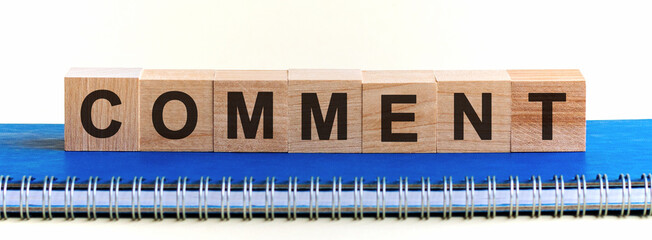Comment - a word made of wooden blocks with black letters, a row of blocks is located on a blue Notepad. White background, front view. Promotion code, promo code concept.