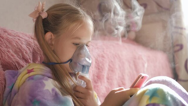Little girl holds inhaler mask at home. Sick kid breathes through a nebulizer. Baby using equipment to treat asthma or bronchitis. Home treatment.