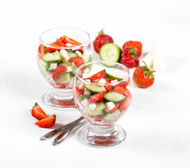 Berry and vegetable salad of strawberries and cucumber with feta cheese in a glass on a light background. 