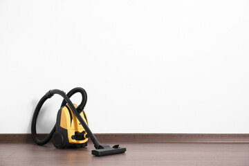 Modern yellow vacuum cleaner on wooden floor near white wall, space for text