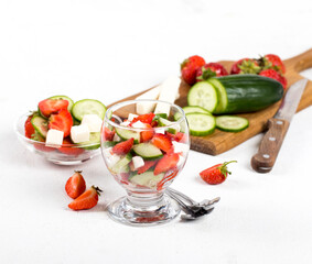 Berry and vegetable salad of strawberries and cucumber with feta cheese in a glass on a light...