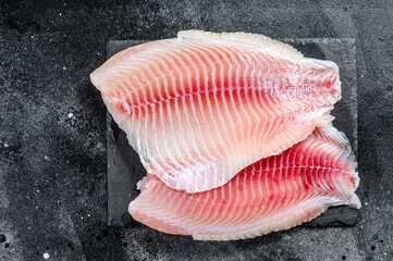 Raw fillet of tilapia on a cutting Board. Black background. Top view