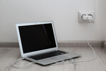 Modern laptop charging from electric socket on floor