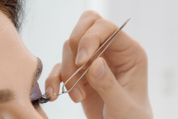 Imposition of artificial eyelashes. Eyelash extensions in a beauty salon. Attaching the lashes with tweezers to the eye.