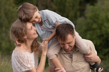 Son sits on the shoulders of his father, mom laughs, happy family, beautiful blonde woman, love, little boy with golden hair, playing with role-stars