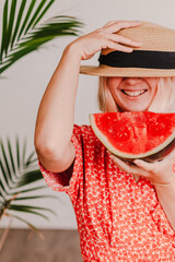 Young beautiful lady in red dress and straw hat is holding juicy watermelon. Red bright color. Green tropical. Summer time vacation. Beach vibes. Hot days. Refreshing red fruit.Pretty millennial woman