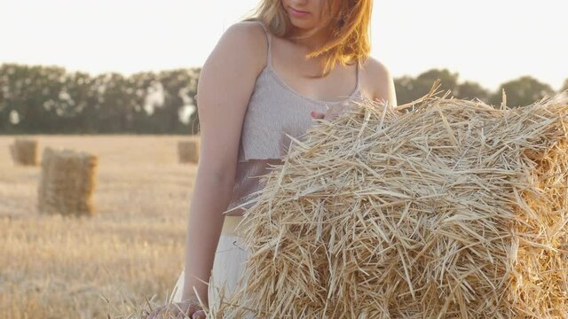 beautiful girl leaned on haystack in field, playing with dry grass, leisure and lifestyle